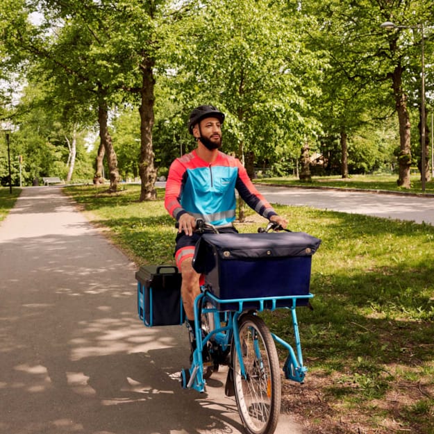 Brevbärare på cykel i grönskande miljö.