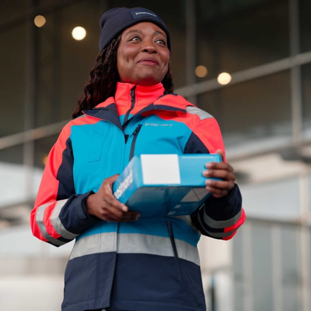 En kvinnlig PostNord-medarbetare håller i ett paket.